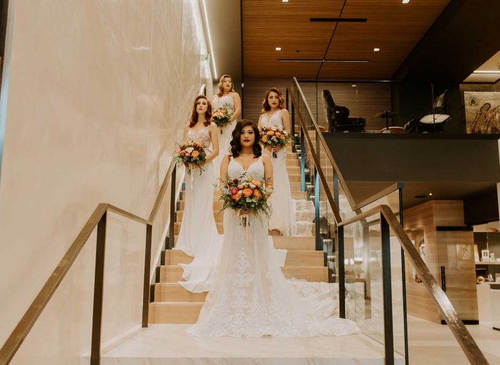 four women in bridal dresses holding flower bouquets on staircase