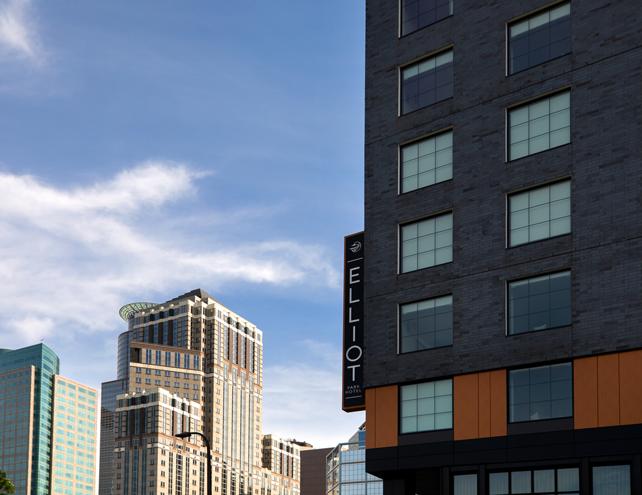 Modern high-rise buildings against a blue sky with scattered clouds; a sign on the foreground building reads Elliot.