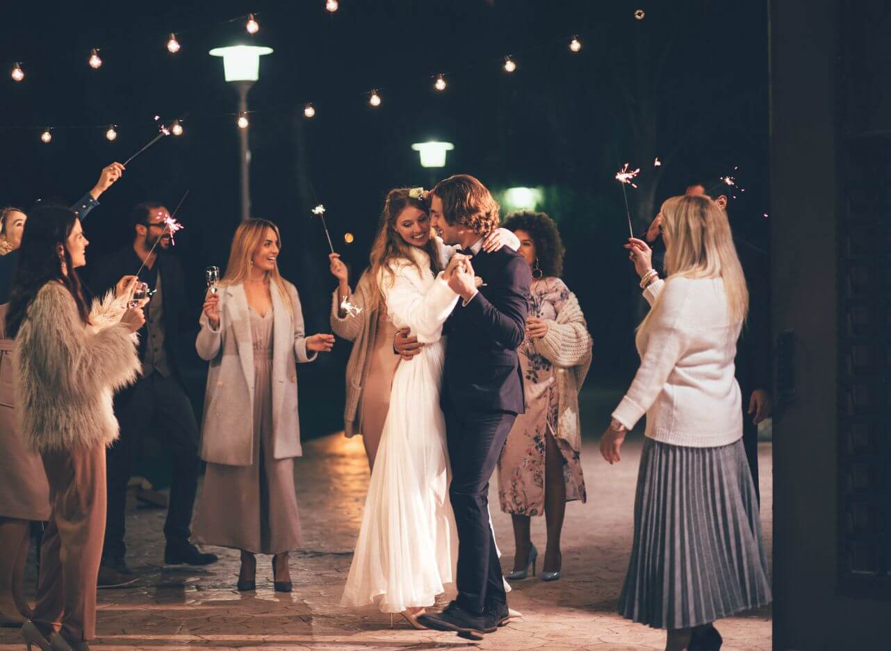 A bride and groom dance outside at night near the Chestnut Ballroom, surrounded by guests holding sparklers beneath glowing string lights.